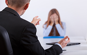 A female professional cries over wrongful dismissal charges as her boss aggressively points at her.